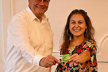 Bürgermeister Thomas Steiner mit Jugendgemeinderätin Samara Sánchez Pöll und einem Klimaticket, das ebenfalls von der Stadt für junge Menschen gefördert wird.