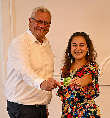 Bürgermeister Thomas Steiner mit Jugendgemeinderätin Samara Sánchez Pöll und einem Klimaticket, das ebenfalls von der Stadt für junge Menschen gefördert wird.