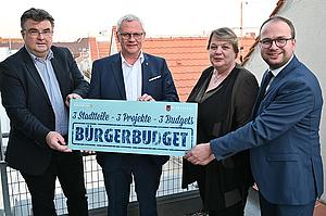 Gruppenfoto von 4 Gemeindevertretern die eine Texttafel zum Bürgerbudget halten.